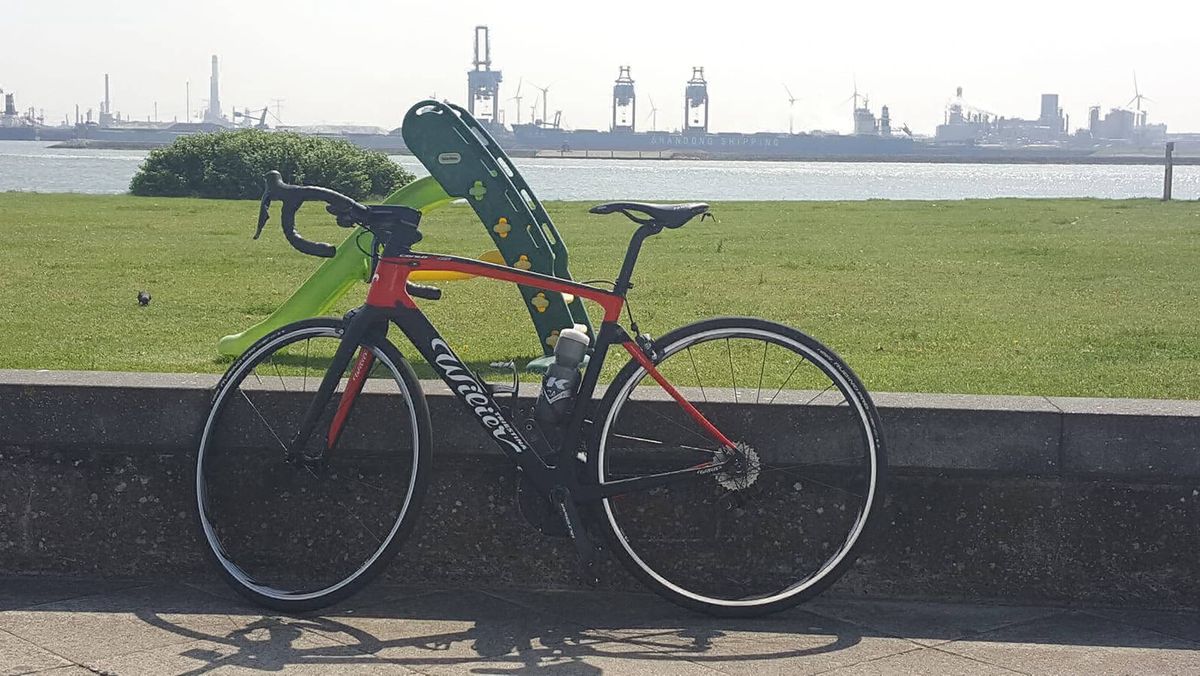 Racefiets aan de waterkant met aangemeerde boten op de achtergrond.