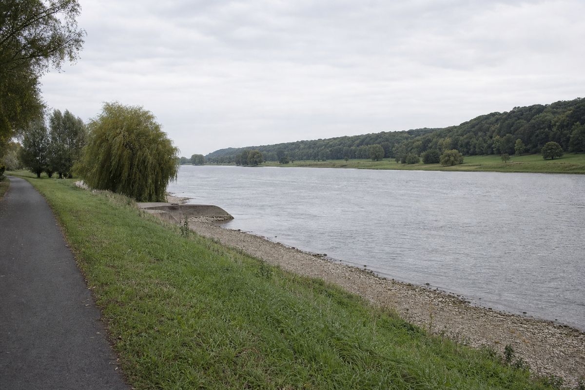 Brede langzaam stromende rivier gezien vanaf het fietspad op de oever, met beboste hellingen aan de overkant.